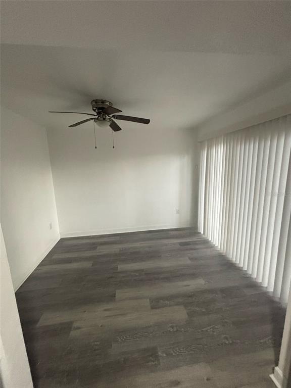An empty room features gray wood-look flooring, white walls, a ceiling fan, and vertical blinds — 5930 VILLAGE CIRCLE UNIT GE, ORLANDO, FL