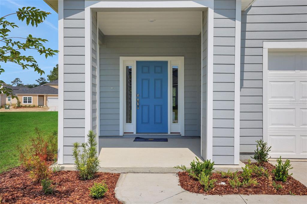 A blue front door with sidelights is centered on the covered porch of a house — 3897 HOLSTEIN WAY, GREEN COVE SPRINGS, FL