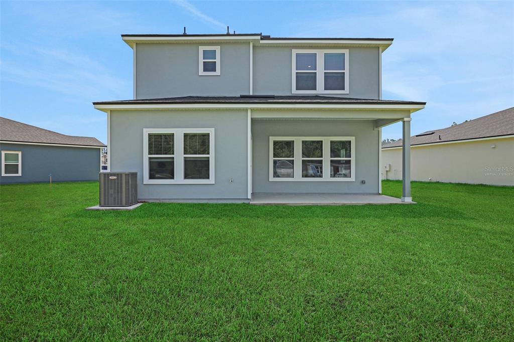 The back exterior of a two-story house features a covered patio and a grassy yard — 3897 HOLSTEIN WAY, GREEN COVE SPRINGS, FL