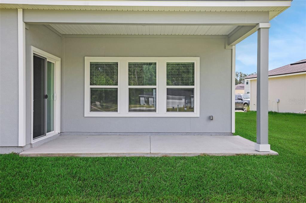 A covered concrete patio sits outside a gray house with a sliding glass door — 3897 HOLSTEIN WAY, GREEN COVE SPRINGS, FL