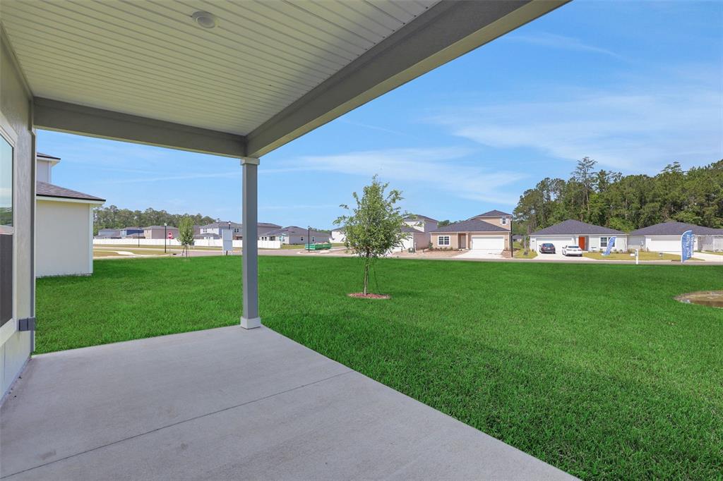 A concrete patio overlooks a large grassy backyard with neighboring houses in the distance — 3897 HOLSTEIN WAY, GREEN COVE SPRINGS, FL