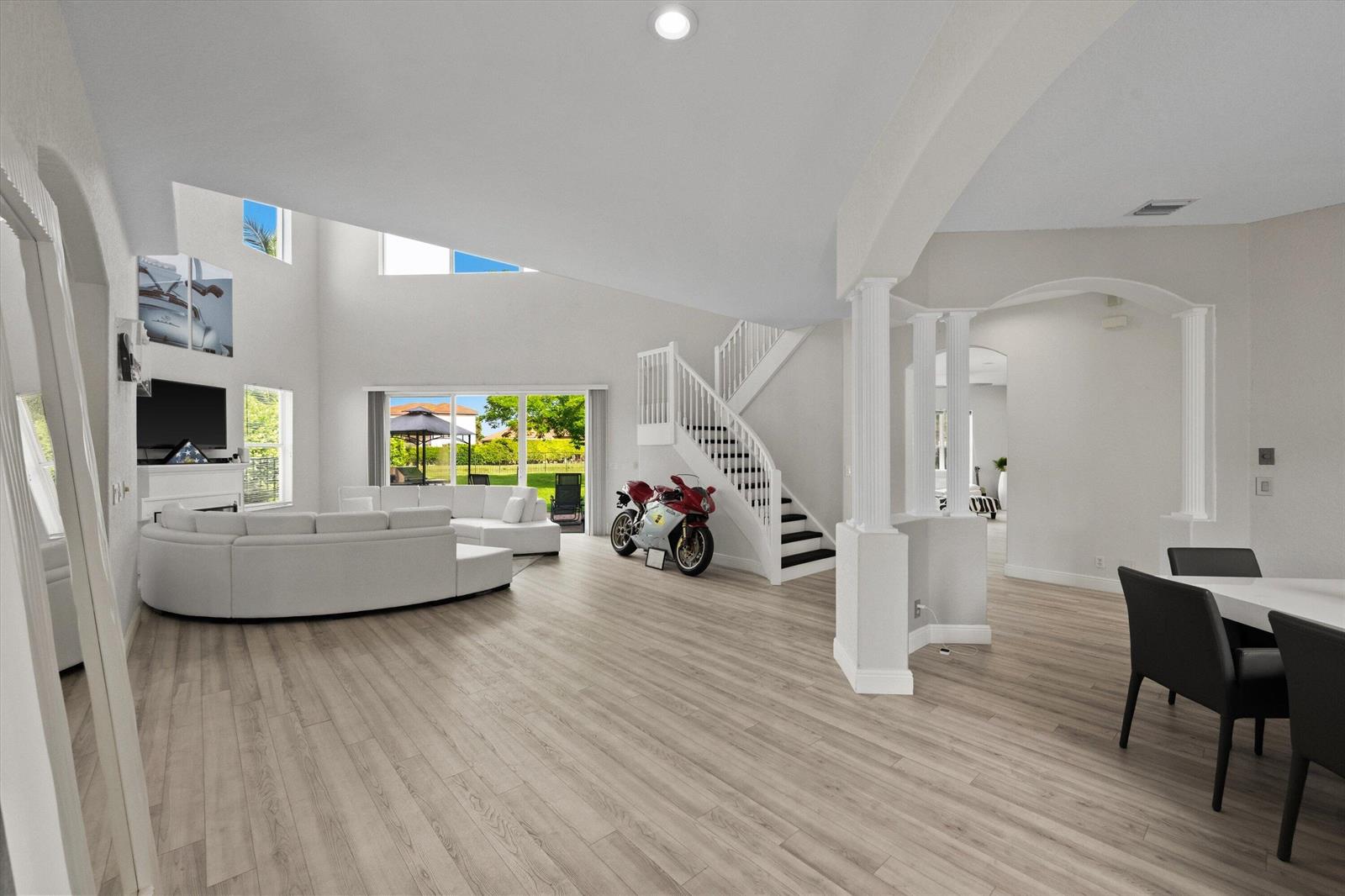 A spacious living room features light wood flooring, a white sectional sofa, and a red motorcycle — 1215 Creekside Drive, Wellington FL 33414, WELLINGTON, FL