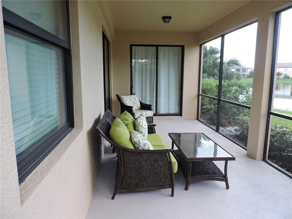 A screened-in patio features wicker furniture, a glass-topped table, and views of a pond — 20201 RAGAZZA CIRCLE UNIT 102, VENICE, FL