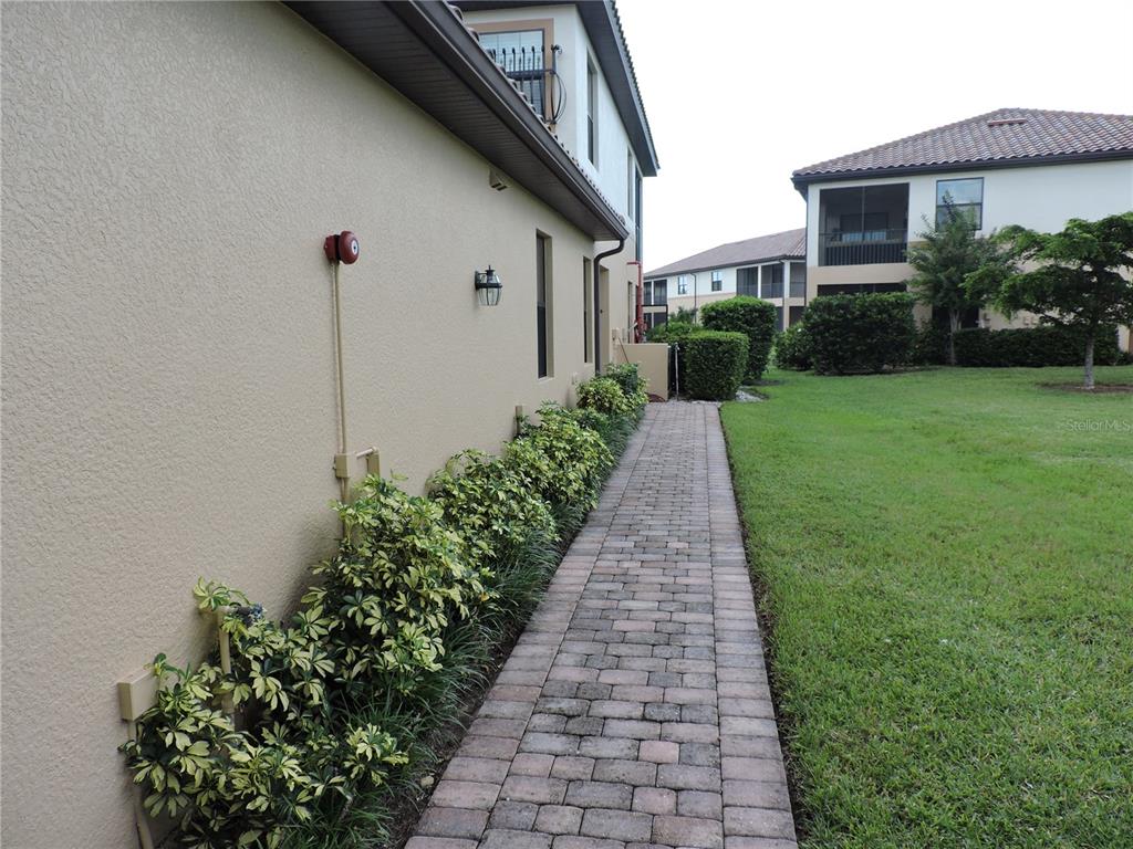 A paved walkway runs alongside a tan building exterior with landscaping and a grassy lawn — 20201 RAGAZZA CIRCLE UNIT 102, VENICE, FL