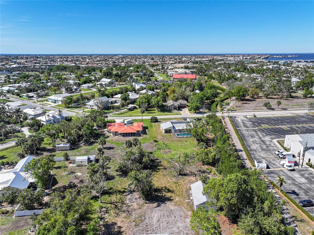 An aerial view shows residential houses, a large parking lot, and surrounding vegetation under a clear sky — 479 GILL STREET, PUNTA GORDA, FL