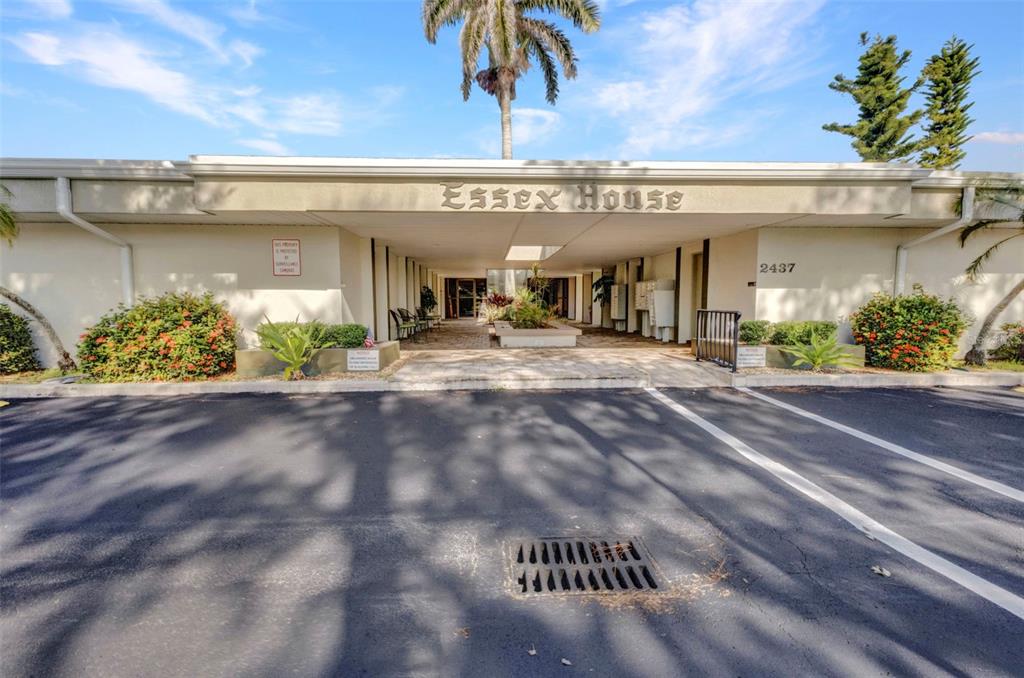 The exterior of a low-rise apartment building features a covered entrance with a palm tree — 2437 HARBOR BOULEVARD UNIT 114, PORT CHARLOTTE, FL