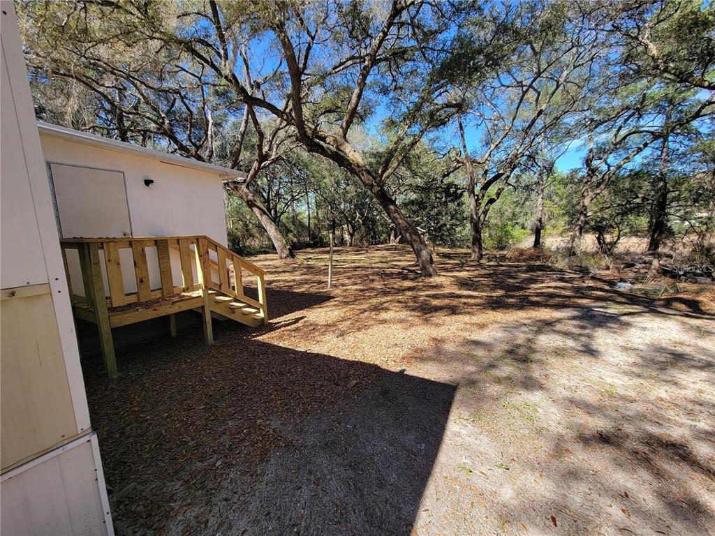 A wooden staircase leads to the side door of a white building near trees — 16625 NE 2ND STREET ROAD, SILVER SPRINGS, FL