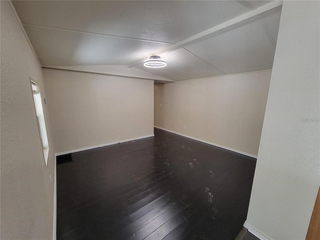 An empty room features dark wood flooring, light-colored walls, and a circular ceiling light — 16625 NE 2ND STREET ROAD, SILVER SPRINGS, FL