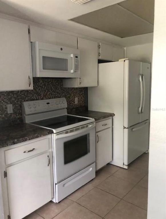 A kitchen features white cabinets, white appliances, a dark countertop, and a mosaic tile backsplash — 6910 S TRASK STREET, TAMPA, FL
