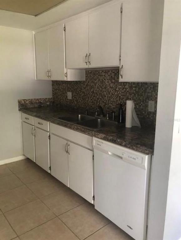 A kitchen features white cabinets, a dark countertop, a mosaic backsplash, and a white dishwasher — 6910 S TRASK STREET, TAMPA, FL