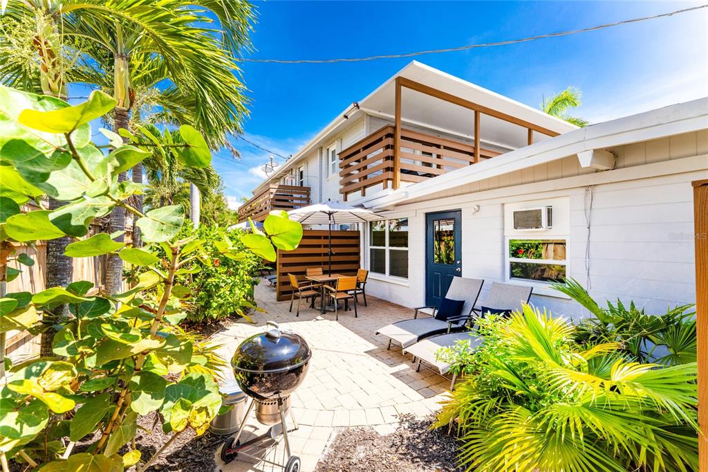 A patio with a grill, outdoor seating, and lounge chairs sits beside a two-story building — 1120 GULF BOULEVARD, ENGLEWOOD, FL