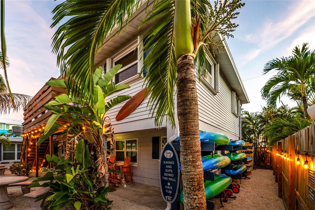 A two-story house exterior features a surfboard, palm trees, and a rack of kayaks — 1120 GULF BOULEVARD, ENGLEWOOD, FL