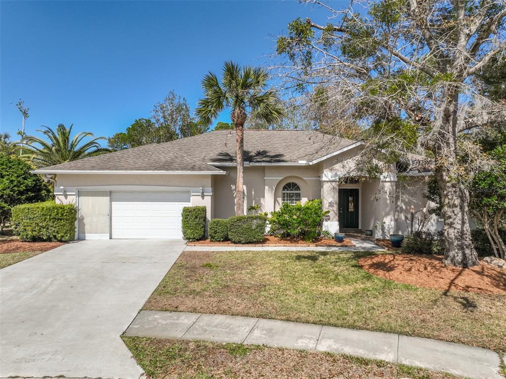 A single-story house with a white garage, beige stucco exterior, and a palm tree — 28 MONTAUK LANE, PALM COAST, FL