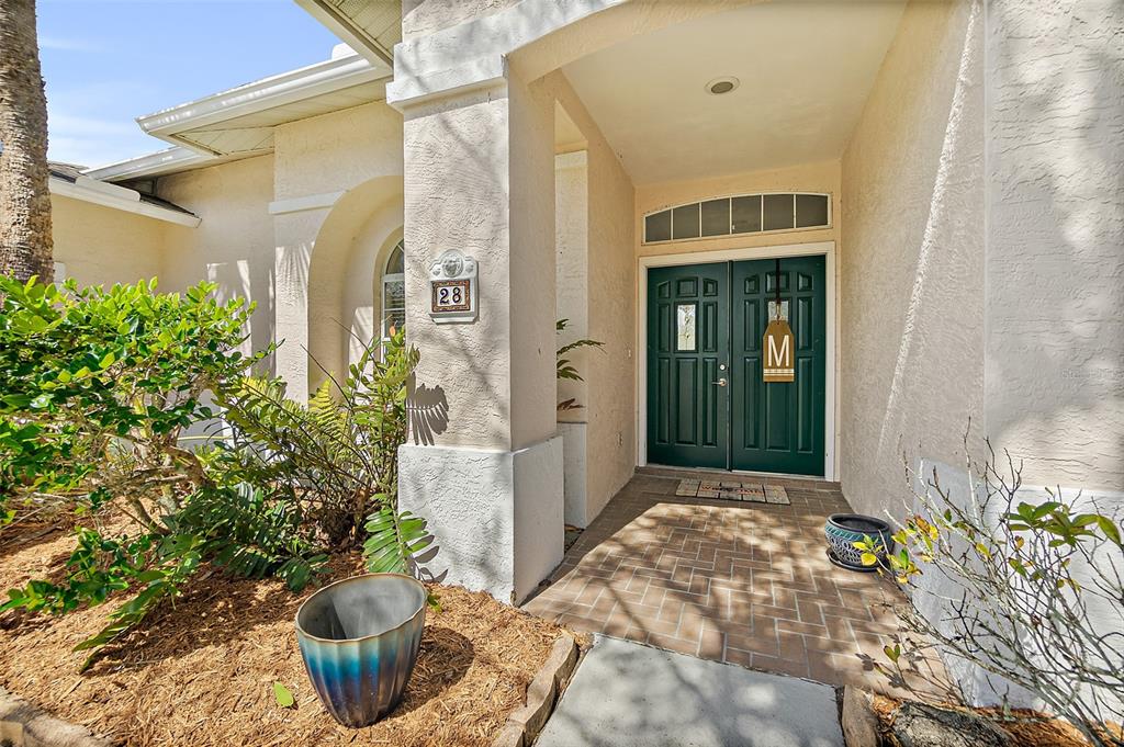 A front entryway features a double green door, a brick porch, and a house number plaque — 28 MONTAUK LANE, PALM COAST, FL