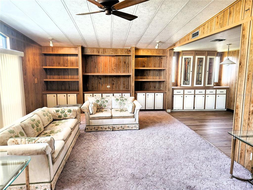 A living room features wood-paneled walls, built-in shelving, a floral sofa, and pink carpeting — 151 LAZY RIVER ROAD, NORTH PORT, FL