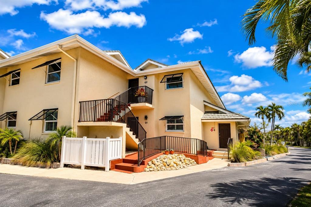 A two-story tan stucco apartment building features an exterior staircase, a white fence, and landscaping — 4660 OCEAN BOULEVARD UNIT Q, SARASOTA, FL