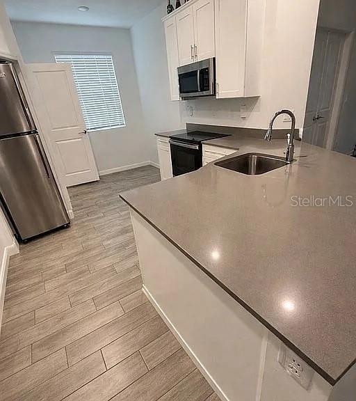 A kitchen features white cabinets, stainless steel appliances, a gray countertop, and wood-look tile flooring — 1104 SAND TRAP COURT, DAYTONA BEACH, FL