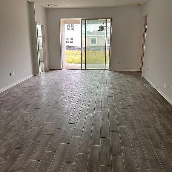 An empty room features gray wood-look tile flooring and a sliding glass door to outside — 1104 SAND TRAP COURT, DAYTONA BEACH, FL
