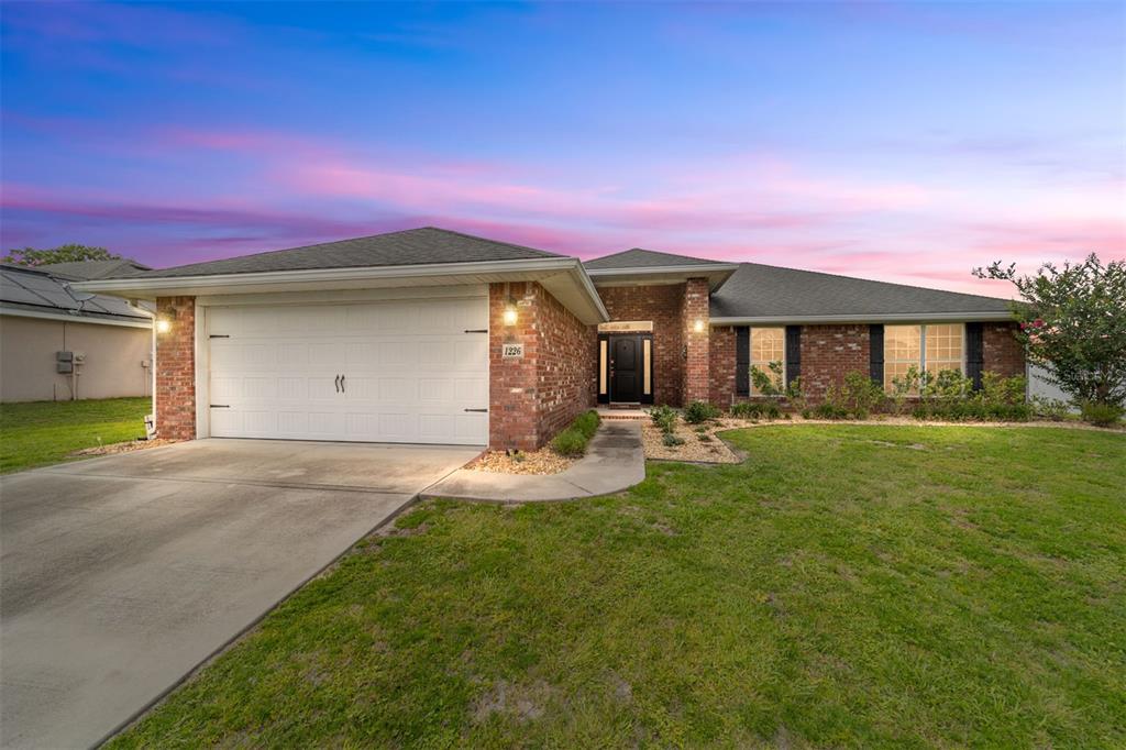 A single-story brick house with a two-car garage and a front lawn at sunset — 1226 SE 65TH CIRCLE, OCALA, FL