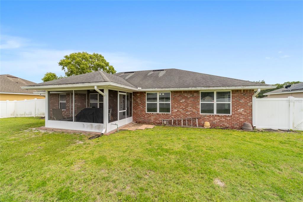 A brick house features a screened-in porch and a large backyard enclosed by white fencing — 1226 SE 65TH CIRCLE, OCALA, FL