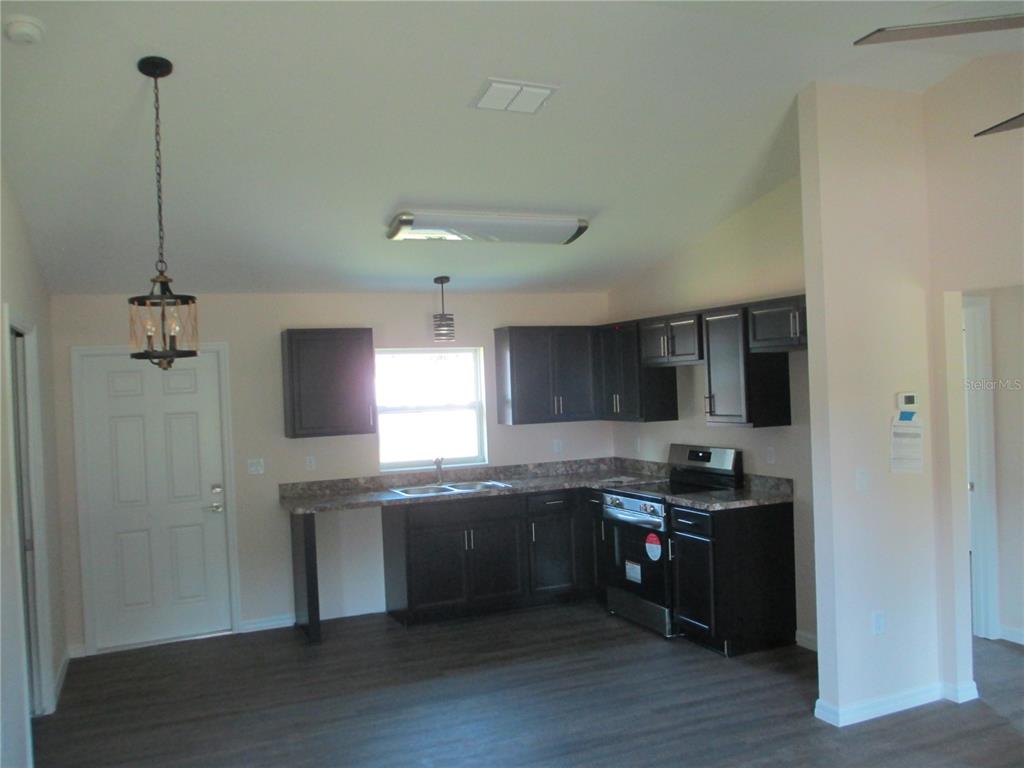 A kitchen features dark wood cabinets, laminate countertops, stainless steel appliances, and dark flooring — 5748 NW 5TH STREET, OCALA, FL