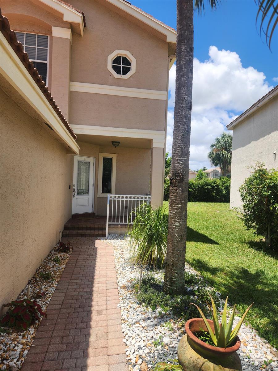 A paved walkway leads to the front entrance of a two-story tan stucco home — 5148 S Aurora Lake Circle, FL 33463, FL