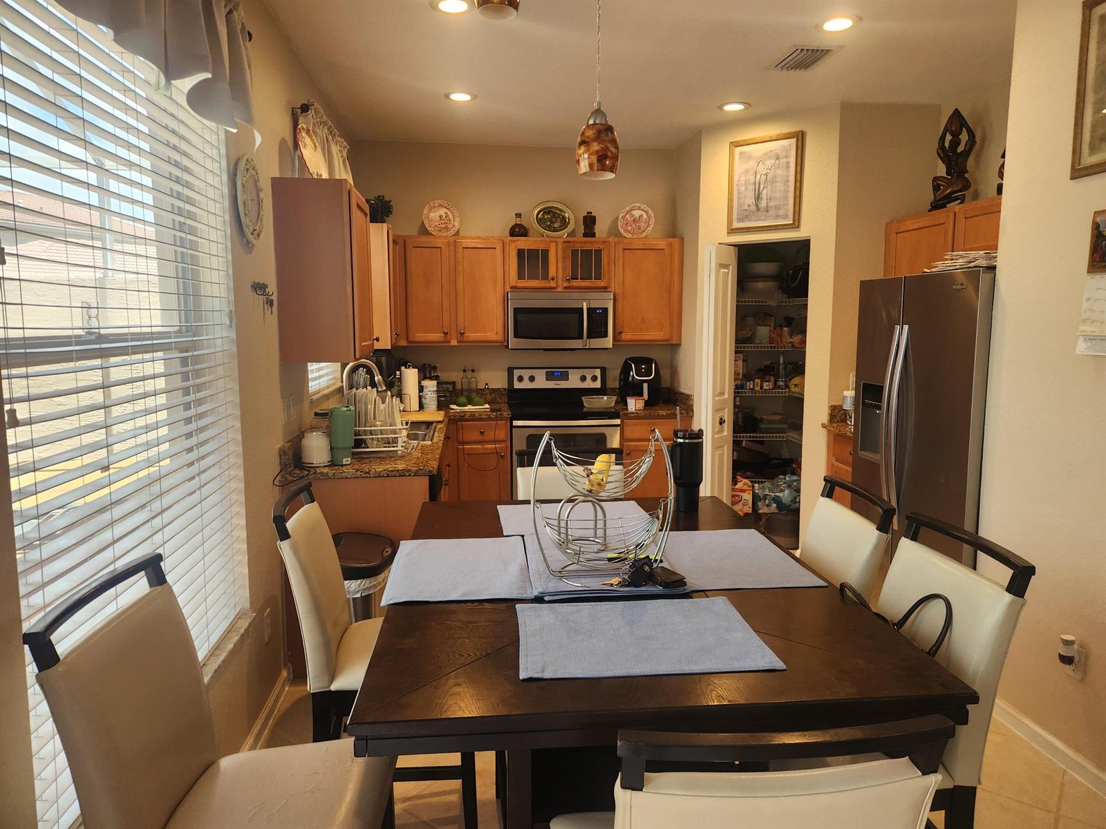 A kitchen with wood cabinets, stainless steel appliances, and a dining table in the foreground — 5148 S Aurora Lake Circle, FL 33463, FL