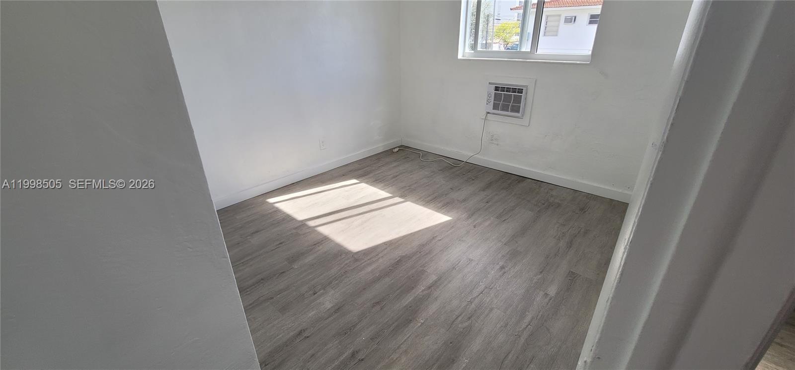 An empty room features white walls, gray wood-look flooring, and a window air conditioning unit — 111 SW 18th Ave, Miami FL 33135, MIAMI, FL
