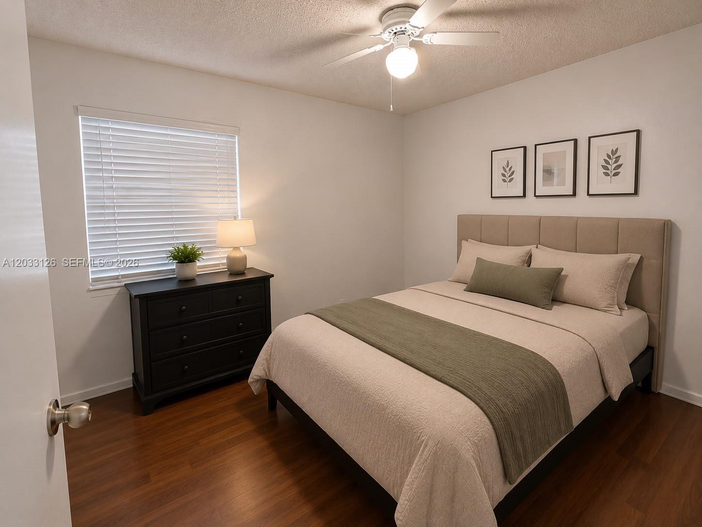 A bedroom features a bed with a tan headboard, a black dresser, and wood flooring — 19831 NW 65th Ct # 0, Hialeah FL 33015, HIALEAH, FL