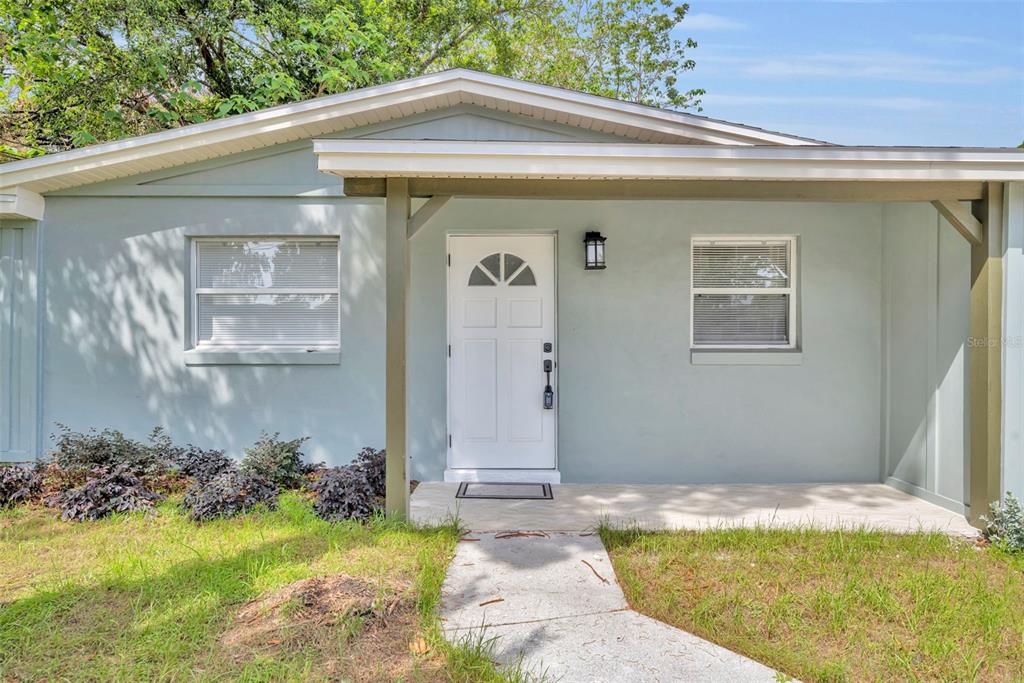 A light blue house exterior features a white front door, a covered porch, and windows — 1224 HELEN STREET, APOPKA, FL