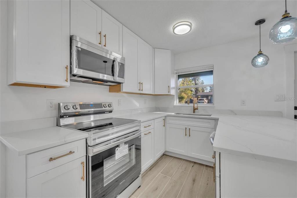 A modern kitchen features white cabinets, stainless steel appliances, a breakfast bar, and light flooring — 1224 HELEN STREET, APOPKA, FL