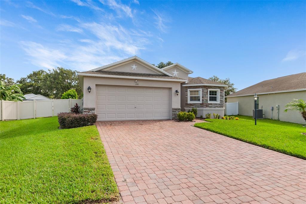 A single-story house with a two-car garage, stone accents, and a brick paver driveway — 110 PROMENADE COURT, AUBURNDALE, FL
