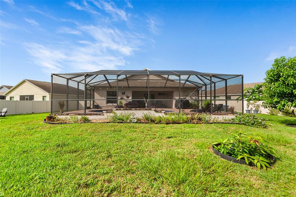A backyard view of a house with a screened-in pool enclosure and a grassy lawn — 110 PROMENADE COURT, AUBURNDALE, FL