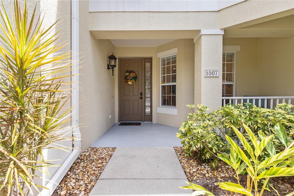 A concrete walkway leads to the front door of a beige house with landscaping — 5507 KEY WEST PLACE UNIT 5507, BRADENTON, FL