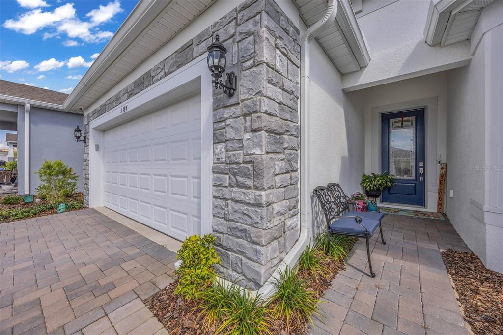 A stone-accented garage and entryway with a blue front door and a metal bench — 1384 ZESTY CITRUS LANE, MINNEOLA, FL