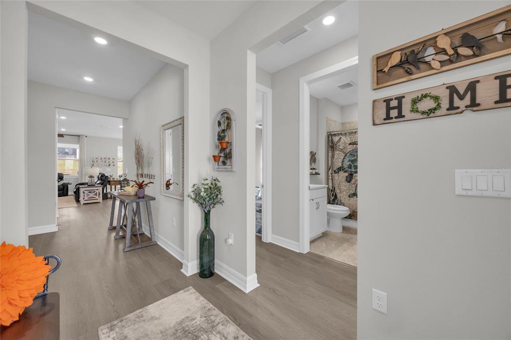 A hallway with light gray walls and wood-look flooring leads to a living area — 1384 ZESTY CITRUS LANE, MINNEOLA, FL