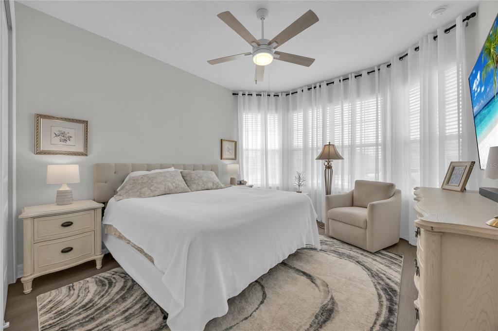 A bedroom features a king bed, a sitting chair, a ceiling fan, and large windows — 1384 ZESTY CITRUS LANE, MINNEOLA, FL