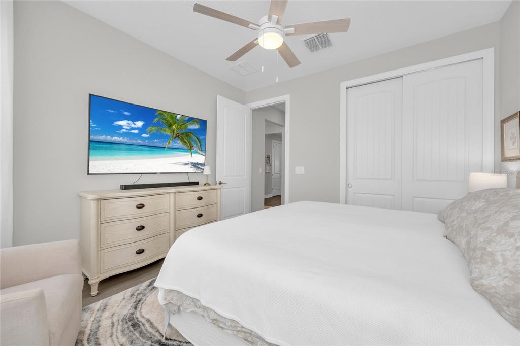 A bedroom features a white dresser, a wall-mounted television, a ceiling fan, and a bed — 1384 ZESTY CITRUS LANE, MINNEOLA, FL
