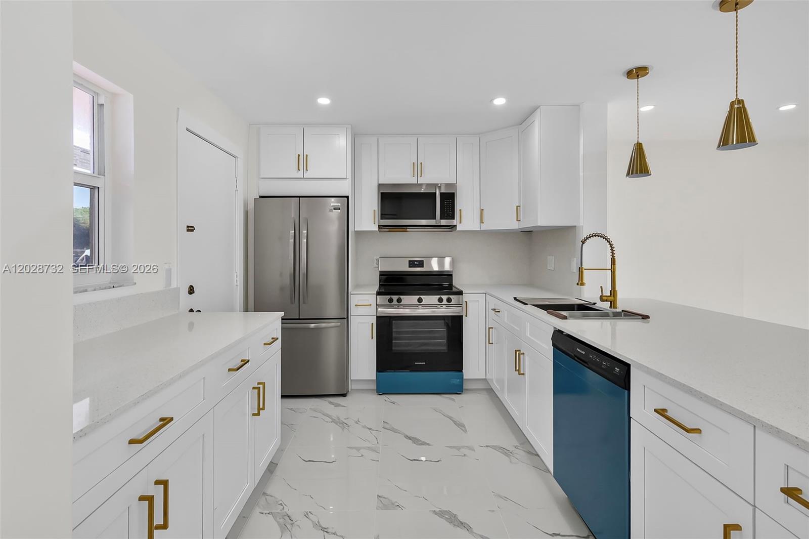 A modern kitchen features white cabinetry, gold hardware, stainless steel appliances, and marble-patterned tile flooring — 201 SE 11th Ter # 102, Dania Beach FL 33004, DANIA BEACH, FL