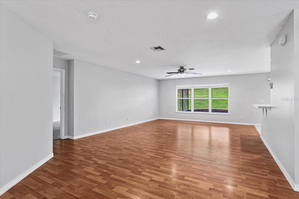 A spacious, empty living room features light gray walls, wood-look flooring, and a ceiling fan — 1882 VALE DRIVE, CLERMONT, FL