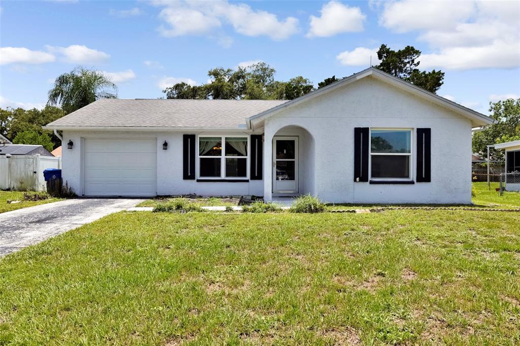 A single-story white house with a garage, black shutters, and a front lawn — 7412 HUMBOLDT AVENUE, NEW PORT RICHEY, FL