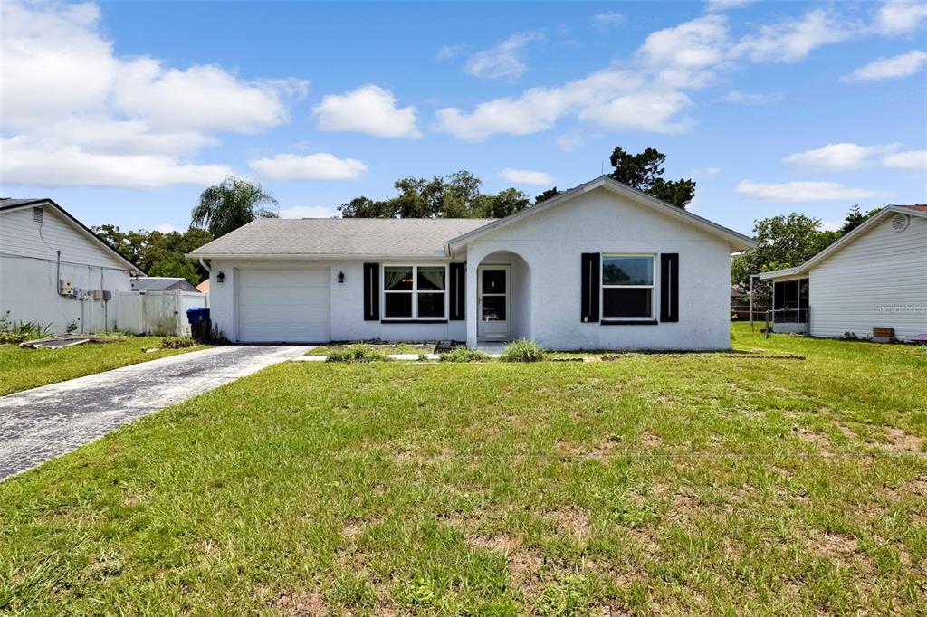 A single-story white house with a garage, front entrance, and a grassy lawn — 7412 HUMBOLDT AVENUE, NEW PORT RICHEY, FL