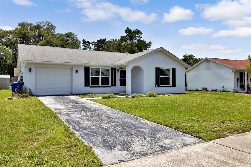 A white, single-story house with a garage and a worn asphalt driveway — 7412 HUMBOLDT AVENUE, NEW PORT RICHEY, FL