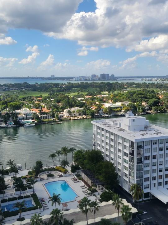 An aerial view shows a waterfront swimming pool, a multi-story building, and a distant cityscape — 5601 Collins Ave # 9, Miami Beach FL 33140, MIAMI BEACH, FL