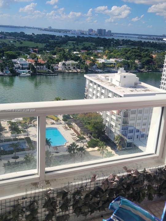 A high-angle view from a balcony overlooks a swimming pool, a waterway, and distant buildings — 5601 Collins Ave # 9, Miami Beach FL 33140, MIAMI BEACH, FL