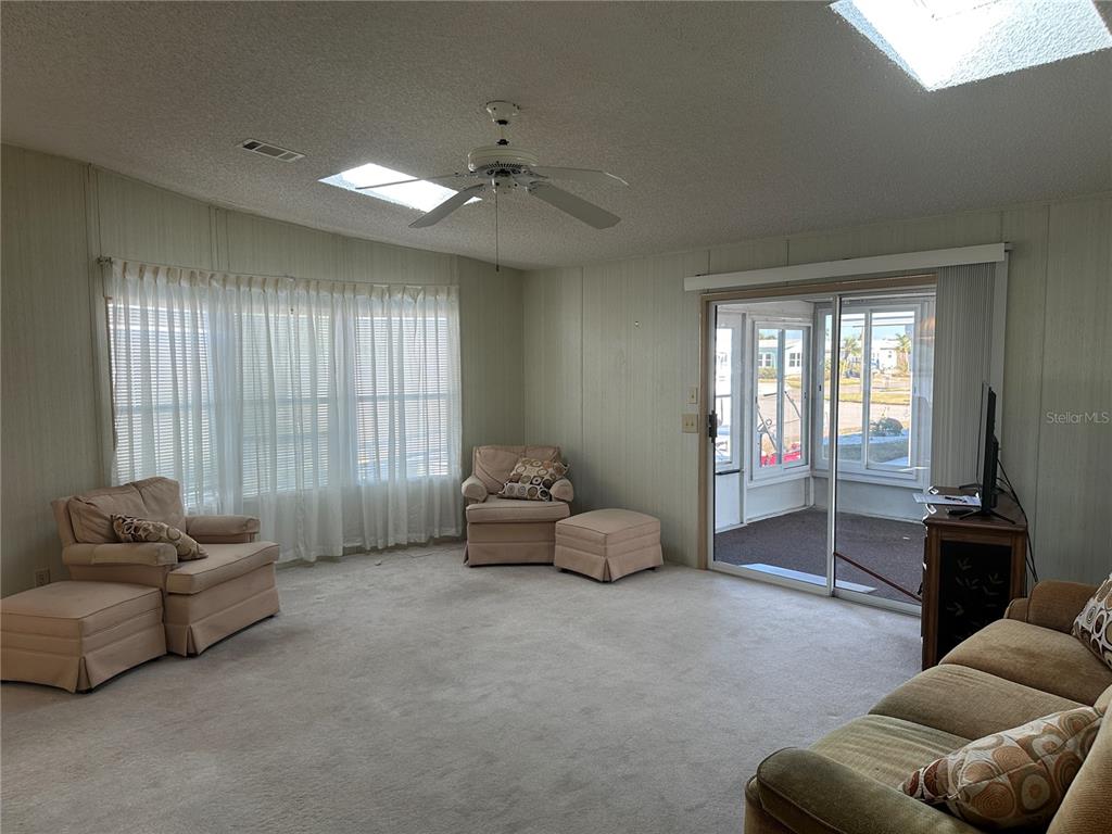 A living room features beige carpet, paneled walls, a ceiling fan, skylights, and sliding glass doors — 449 LANDSEDGE DRIVE, NORTH PORT, FL
