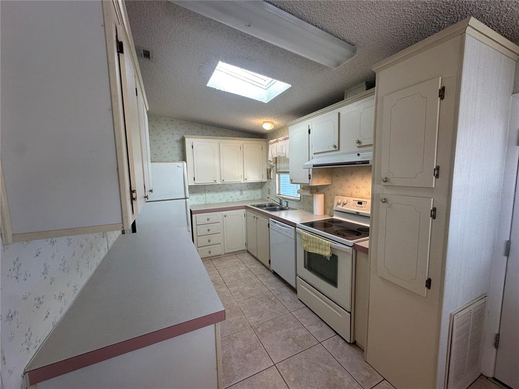A kitchen features white cabinets, a skylight, tile flooring, and white appliances — 449 LANDSEDGE DRIVE, NORTH PORT, FL
