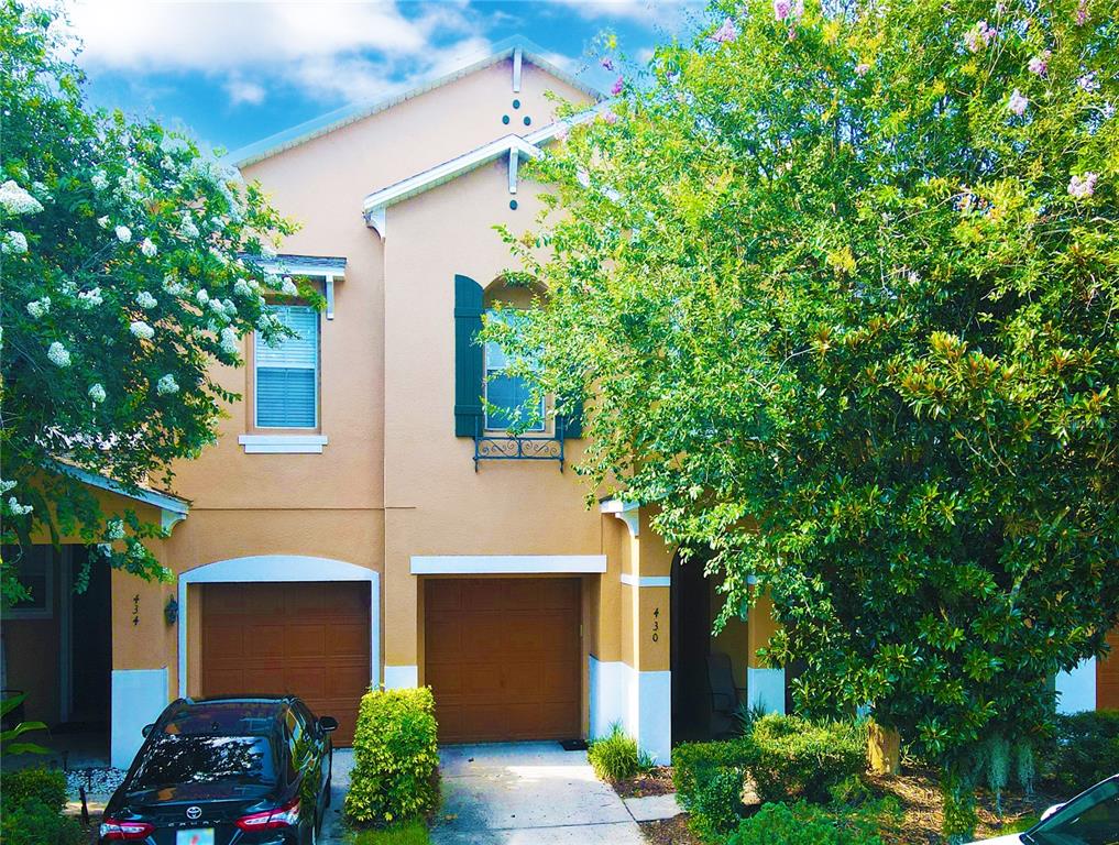 The exterior of a two-story tan townhouse features two garage doors and green shutters — 430 PENNY ROYAL PLACE, OVIEDO, FL