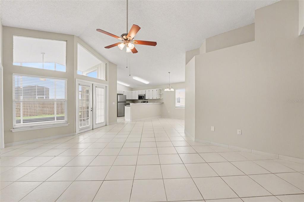 An open-concept living and dining area features white tile floors, vaulted ceilings, and a kitchen — 204 KINGSHILL COURT SE, WINTER HAVEN, FL