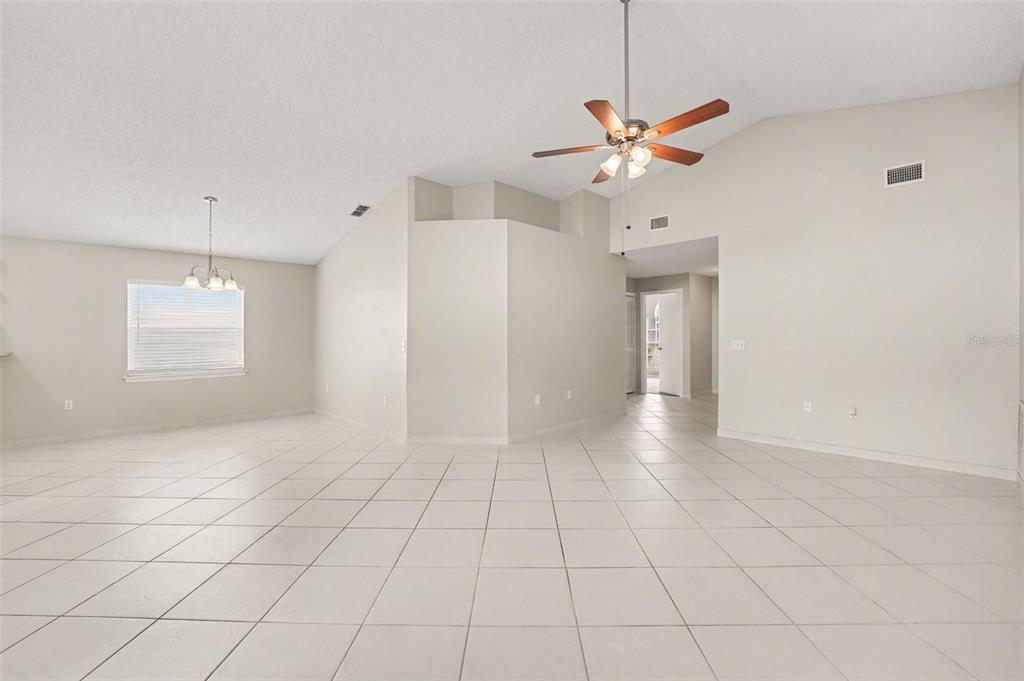 A spacious, empty living area with light-colored tile flooring, vaulted ceilings, and a ceiling fan — 204 KINGSHILL COURT SE, WINTER HAVEN, FL